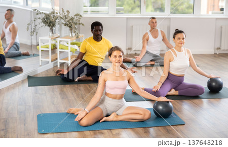 Multinational athletes sitting on floor in asana pigeon do body tilts to side, use fitball 137648218