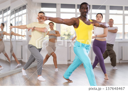 Positive African american man dancing and training movements Latin dance bachata during group class in choreography studio 137648467