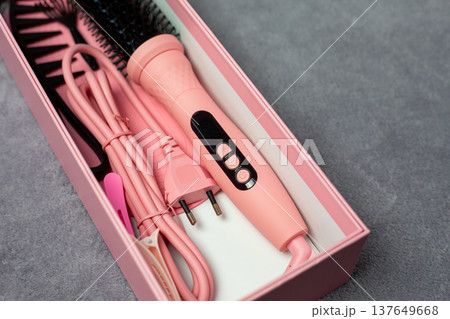 Box containing pink electric multi styler brush for hair styling. Everything in pink for pink lovers. Rich pink electric brush for girls and hair care. Complete set for creating perfect hairstyle 137649668