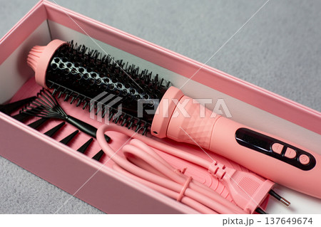 High-tech pink electric multi-styler for hair. Cylindrical brush with heating function, comb, and clips on neutral surface. Modern beauty gadget for flawless styling 137649674