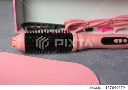 Multifunctional hair styling tool that combines the functions of several devices. Round, heated brush in pink case for women. Cute color for hairstyling device. Beauty concept 137649679