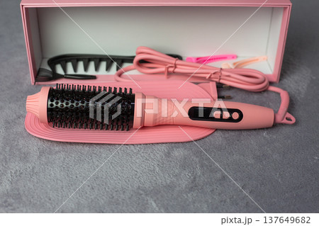 Stylish pink electric hair multi styler with matching comb and clips. Beautifully packaged in pink box on grey surface. Aesthetic beauty tool for fashion-conscious women 137649682