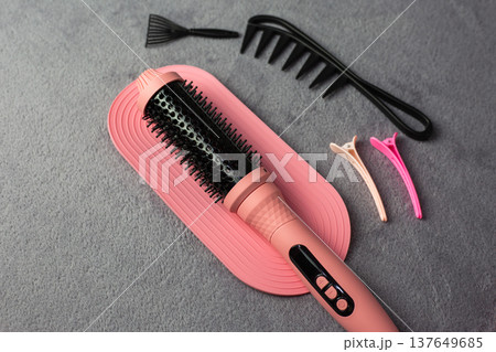 Hair styling tools such as a round brush, combs, and hair clips are neatly arranged on a pink mat with a gray background, suitable for beauty and grooming applications 137649685