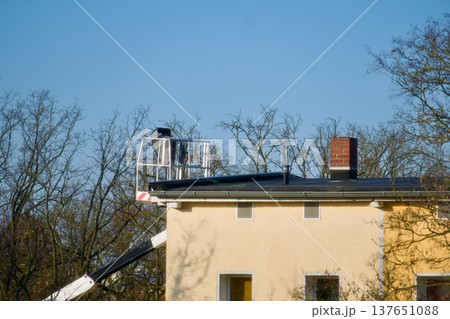 A professional chimney sweep working from an aerial lift platform to inspect and maintain a brick chimney on a residential house roof. A clear view of the specialist at work, emphasizing safety A professional chimney sweep working from an aerial lift platform to inspect and maintain a brick chimney on a residential house roof. A clear view of the specialist at work, emphasizing safety 137651088