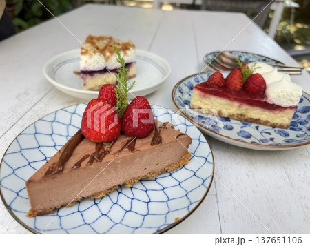 Assortment of Gourmet Cheesecake Slices with Fresh Strawberries and Chocolate on White Table Assortment of Gourmet Cheesecake Slices with Fresh Strawberries and Chocolate on White Table 137651106
