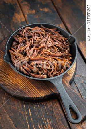 Smoked pulled beef brisket in cast iron skillet, juicy shredded barbecue meat with rosemary on rustic wooden table. Smoked pulled beef brisket in cast iron skillet, juicy shredded barbecue meat with rosemary on rustic wooden table. 137651269