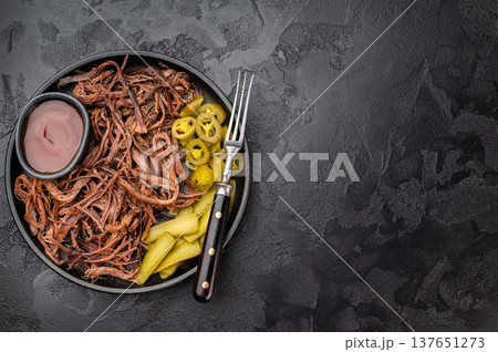 Pulled beef brisket with barbecue sauce, pickles and jalapeno in skillet on dark background, top view with copy space.. 137651273