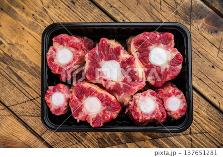 Fresh uncooked mutton lamb oxtail cuts with marrow bones packaged in tray, overhead composition on wooden background 137651281