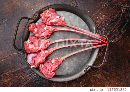 Raw lamb cutlets on bone in cast iron skillet with herbs warm dark background top view butcher meat copy space 137651282