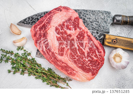 Premium raw ribeye beef steak with intense marbling and thick fat cap. Rustic butcher style on light stone background. 137651285