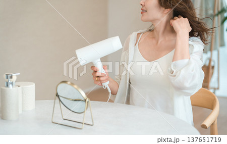 ヘアドライヤーでヘアブロー・髪の毛を乾かす女性（ヘアケア） 137651719