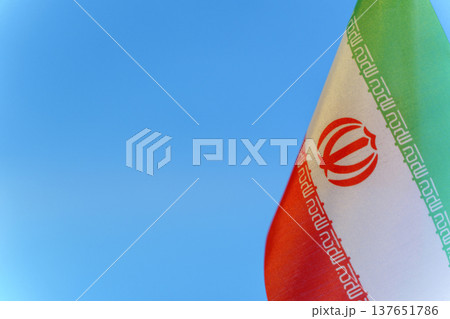 Iran flag against a blue sky background symbolizing political tension and crisis. Close-up view of the Iranian flag representing current geopolitical conflicts, social unrest, and international 137651786
