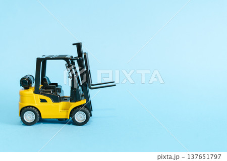 Forklift truck isolated on a blue background as a logic concept of warehouse storage. Conceptual photography showing a miniature toy loader symbolizing supply chain and logistics management with 137651797