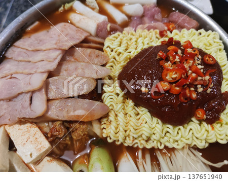 A Korean-style spicy noodle hot pot topped with gochujang chili paste, sliced meat, tofu, and vegetables, representing homemade street food and restaurant-style Korean cuisine A Korean-style spicy noodle hot pot topped with gochujang chili paste, sliced meat, tofu, and vegetables, representing homemade street food and restaurant-style Korean cuisine 137651940
