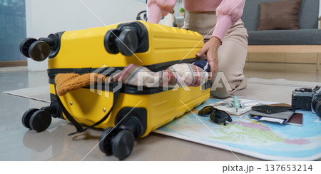 Final Touches. Woman zipping up yellow suitcase after packing. 137653214