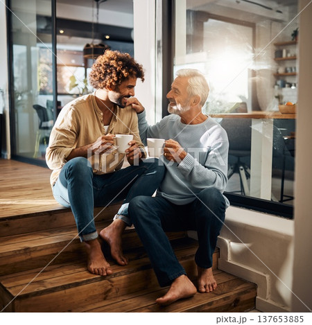 Two men sit on wooden steps, enjoying coffee together in a bright indoor space during morning time, sharing smiles and laughter Two men sit on wooden steps, enjoying coffee together in a bright indoor space during morning time, sharing smiles and laughter 137653885