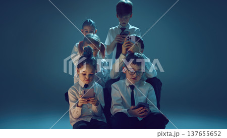Children using smartphones together in neon studio symbolizing digital dependence Children using smartphones together in neon studio symbolizing digital dependence 137655652