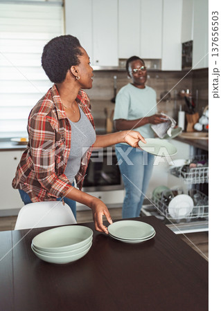 Two Young Women Arranging Dishes on the Table After Emptying the Dishwasher in a Modern Kitchen Two Young Women Arranging Dishes on the Table After Emptying the Dishwasher in a Modern Kitchen 137656503