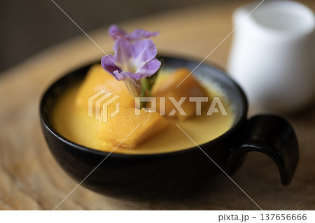 A mango mousse pudding in a cup sits on a table in the cafe. 137656666