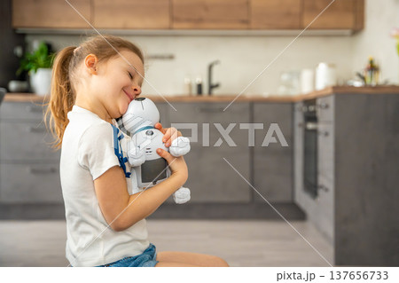 Child hugging robotic dog with affection while sitting on sofa at home. Emotional attachment and digital companionship in modern family life. 137656733
