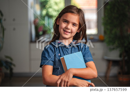Portrait of smiling schoolgirl holding books at home Portrait of smiling schoolgirl holding books at home 137657599