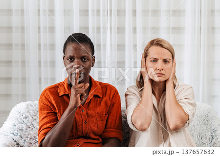 Woman making silence gesture and another covering ears Woman making silence gesture and another covering ears 137657632