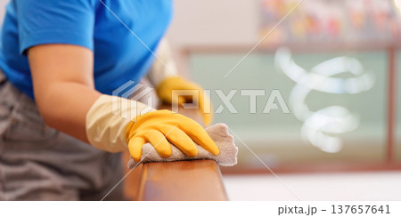 Housekeeping. Woman cleaning a wooden railing with a cloth. Housekeeping. Woman cleaning a wooden railing with a cloth. 137657641