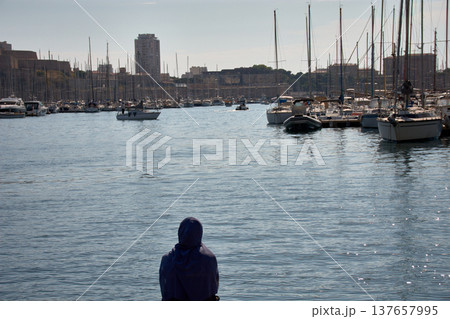 Woman wearing a hijab observes the boats and the horizon from the dock in Marseille, surrounded by water and masts on a sunny day 137657995
