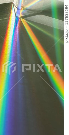 Phone photo of a triangular prism in sunlight creating rainbow lines. Abstract light scene showing color dispersion, geometry, and playful visual effects. 137658594
