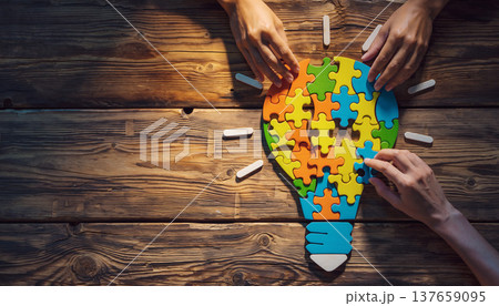 Hands work together to assemble pieces of a colorful puzzle shaped like a light bulb on a wooden table during a creative activity 137659095