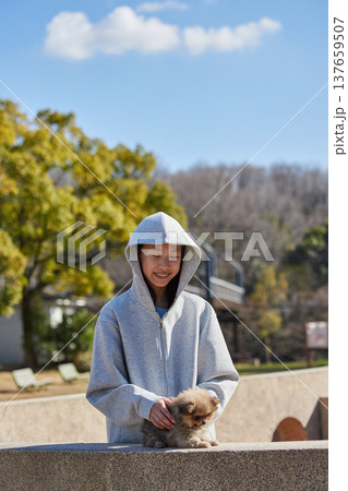 春の晴天の公園で可愛いポメラニアンの子犬と遊んでいる十代の女の子の姿 春の晴天の公園で可愛いポメラニアンの子犬と遊んでいる十代の女の子の姿 137659507