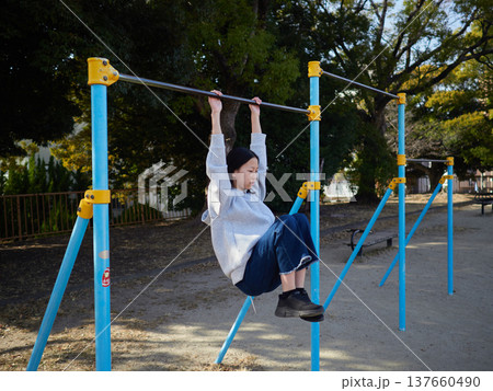 春の昼の公園で楽しく鉄棒で遊んでいる十代の女の子の姿 春の昼の公園で楽しく鉄棒で遊んでいる十代の女の子の姿 137660490