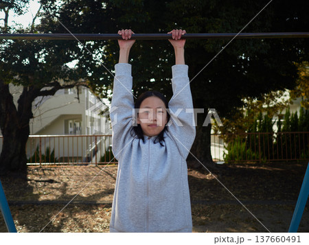 春の昼の公園で楽しく鉄棒で遊んでいる十代の女の子の姿	 137660491
