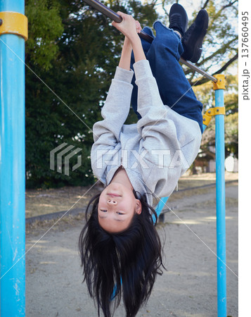 春の昼の公園で楽しく鉄棒で遊んでいる十代の女の子の姿	 137660495