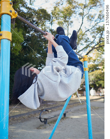 春の昼の公園で楽しく鉄棒で遊んでいる十代の女の子の姿	 137660496