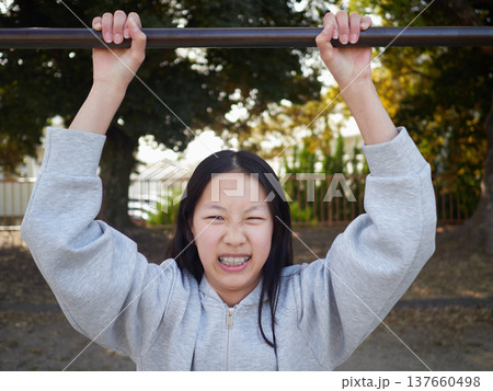 春の昼の公園で楽しく鉄棒で遊んでいる十代の女の子の姿 春の昼の公園で楽しく鉄棒で遊んでいる十代の女の子の姿 137660498