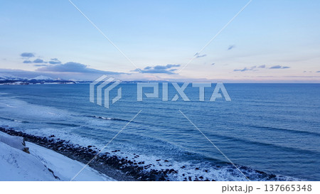 A view showcases the snowy Pacific coastline of the Kuril Islands, featuring striking black volcanic sand and a distant volcano. A view showcases the snowy Pacific coastline of the Kuril Islands, featuring striking black volcanic sand and a distant volcano. 137665348