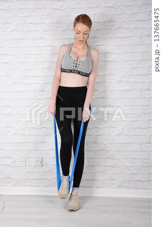 Tall, attractive redhead girl in black leggings and a grey sports bra, exercising at the gym Tall, attractive redhead girl in black leggings and a grey sports bra, exercising at the gym 137665475