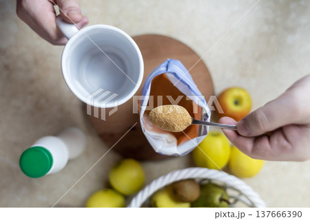 Person adding apple fiber powder to a glass of yogurt, surrounded by fresh apples and walnuts. Healthy prebiotic supplement for gut health, digestion and weight management. 137666390