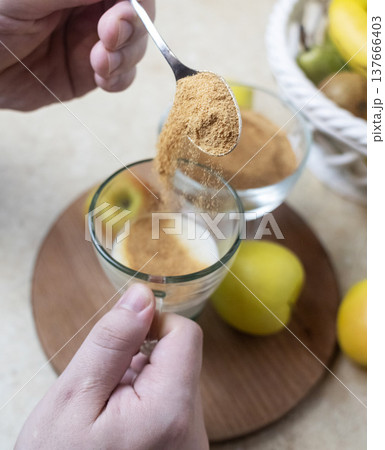 Person adding apple fiber powder to a glass of yogurt, surrounded by fresh apples and walnuts. Healthy prebiotic supplement for gut health, digestion and weight management. Person adding apple fiber powder to a glass of yogurt, surrounded by fresh apples and walnuts. Healthy prebiotic supplement for gut health, digestion and weight management. 137666403