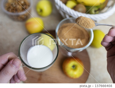 Person adding apple fiber powder to a glass of yogurt, surrounded by fresh apples and walnuts. Healthy prebiotic supplement for gut health, digestion and weight management. Person adding apple fiber powder to a glass of yogurt, surrounded by fresh apples and walnuts. Healthy prebiotic supplement for gut health, digestion and weight management. 137666408
