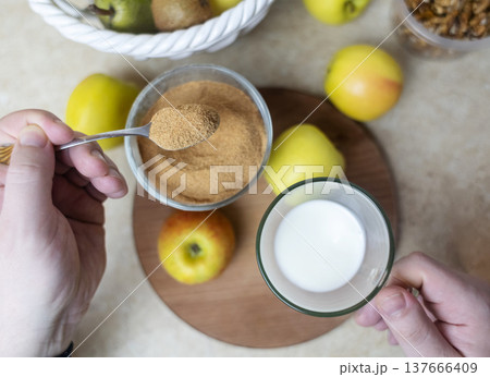 Person adding apple fiber powder to a glass of yogurt, surrounded by fresh apples and walnuts. Healthy prebiotic supplement for gut health, digestion and weight management. Person adding apple fiber powder to a glass of yogurt, surrounded by fresh apples and walnuts. Healthy prebiotic supplement for gut health, digestion and weight management. 137666409