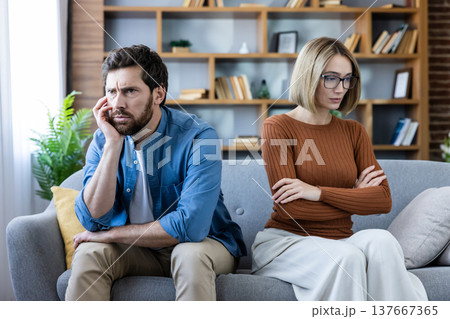 Unhappy couple sitting separately on a sofa, facing away from each other and showing sadness and anger after a relationship problem or disagreement at home 137667365