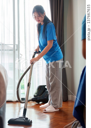 Home Cleaning. Young woman vacuuming the floor in a bright living room. 137667635