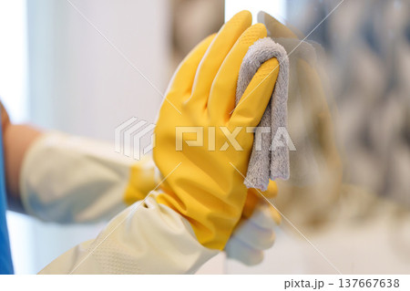 Home Cleaning. Close-up of hands with yellow gloves wiping a glass surface. 137667638