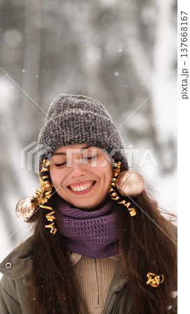 A beautiful young woman in winter clothes is happily spending her free time in a snowy forest. She enjoys the first snow. Active winter recreation. 137668167