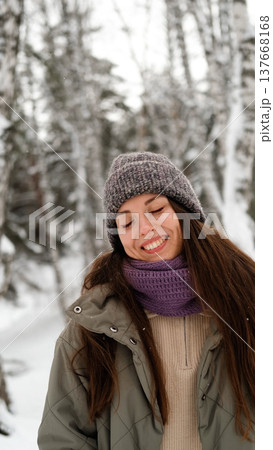A beautiful young woman in winter clothes is happily spending her free time in a snowy forest. She enjoys the first snow. Active winter recreation. 137668168