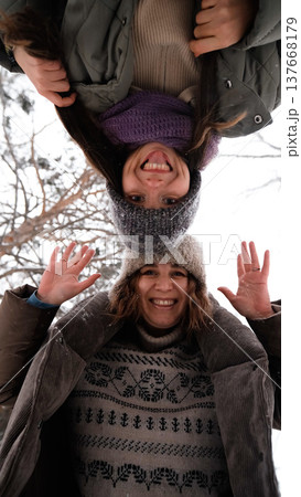 Two cheerful female friends are having fun and laughing in a winter park. The camera is facing upwards. Two cheerful female friends are having fun and laughing in a winter park. The camera is facing upwards. 137668179