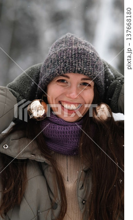A beautiful young woman in winter clothes is happily spending her free time in a snowy forest. She enjoys the first snow. Active winter recreation. 137668180