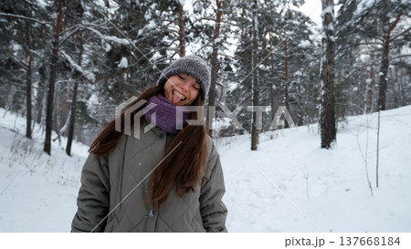 A beautiful young woman in winter clothes is happily spending her free time in a snowy forest. She enjoys the first snow. Active winter recreation. 137668184